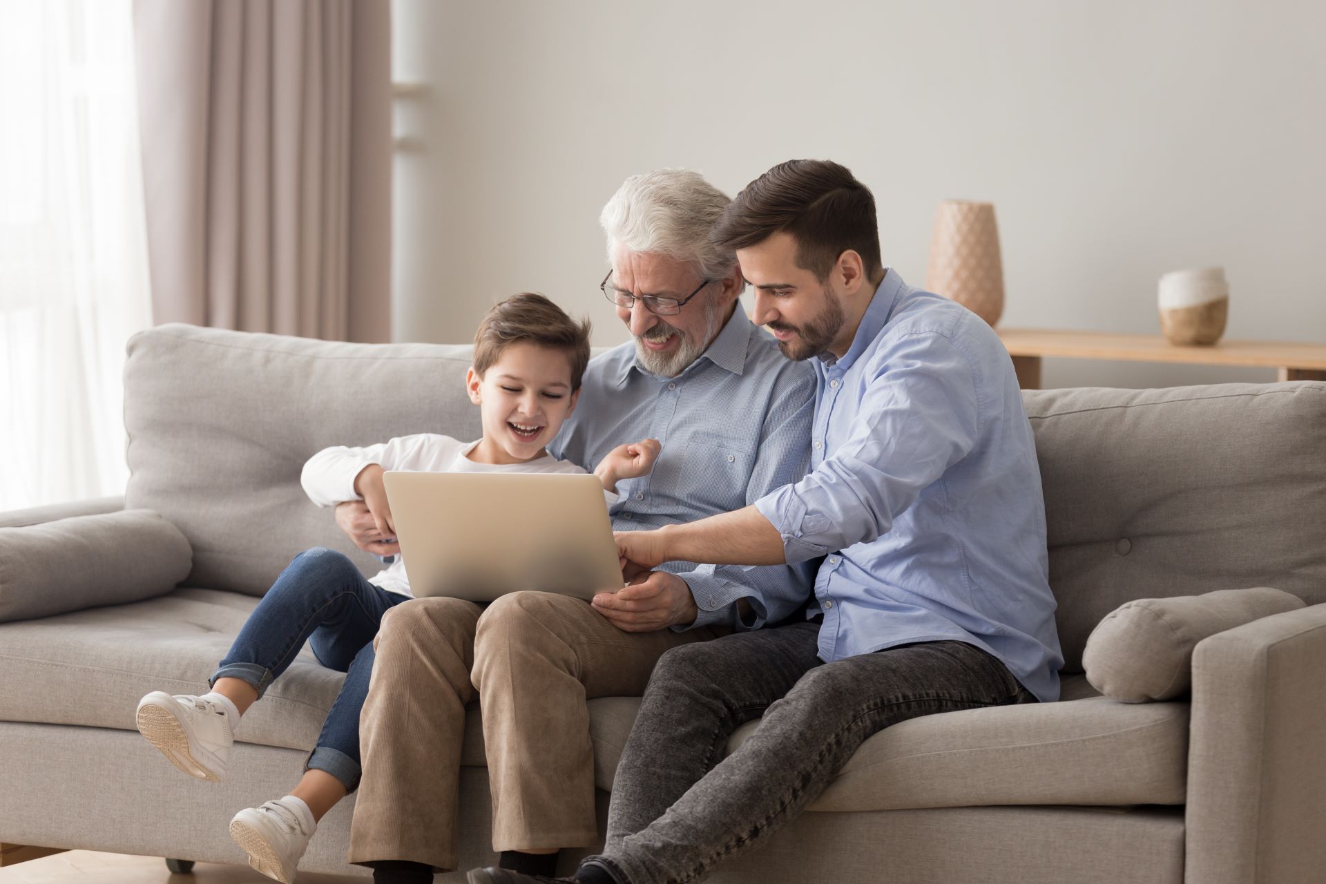 A grandfather using a laptop with his adult son and grandchild